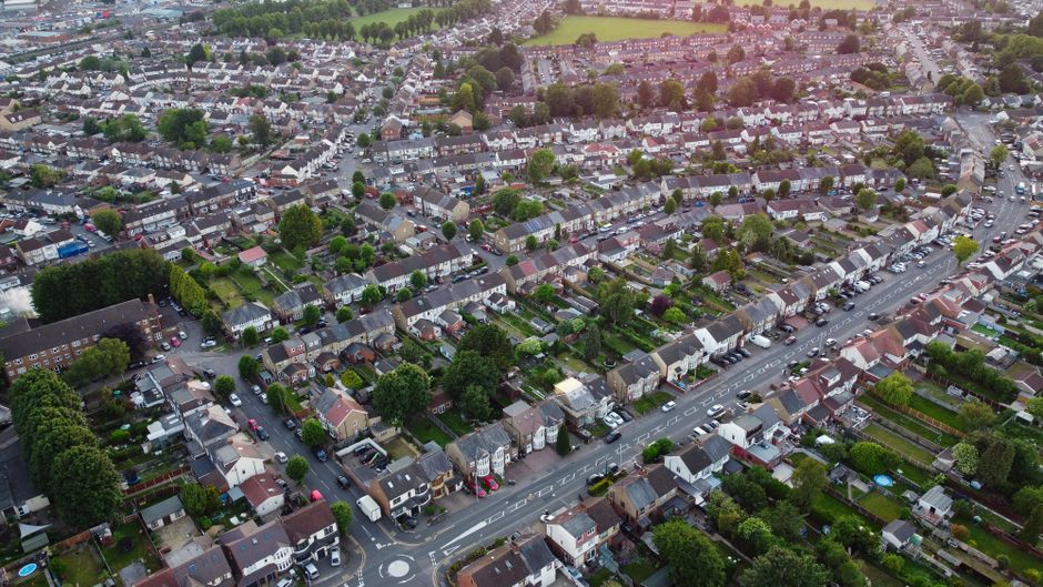 An aerial view of a residential suburban neighbourhood showing multiple rows of terraced and semi-detached houses with brick and tile exteriors. The houses are arranged along winding, narrow streets,